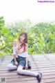 A woman sitting on a wooden deck in a pink top and skirt.