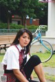 A woman in a school uniform sitting on a bench next to a bike.