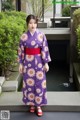 A woman in a purple kimono standing in front of a pond.