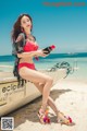 A woman in a red bikini sitting on a boat on the beach.