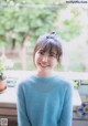 A young woman in a blue sweater smiles at the camera.