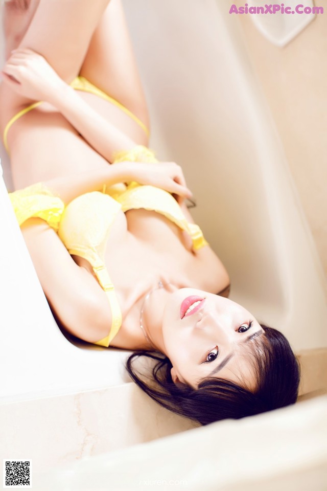 A woman in a yellow lingerie laying in a bathtub.